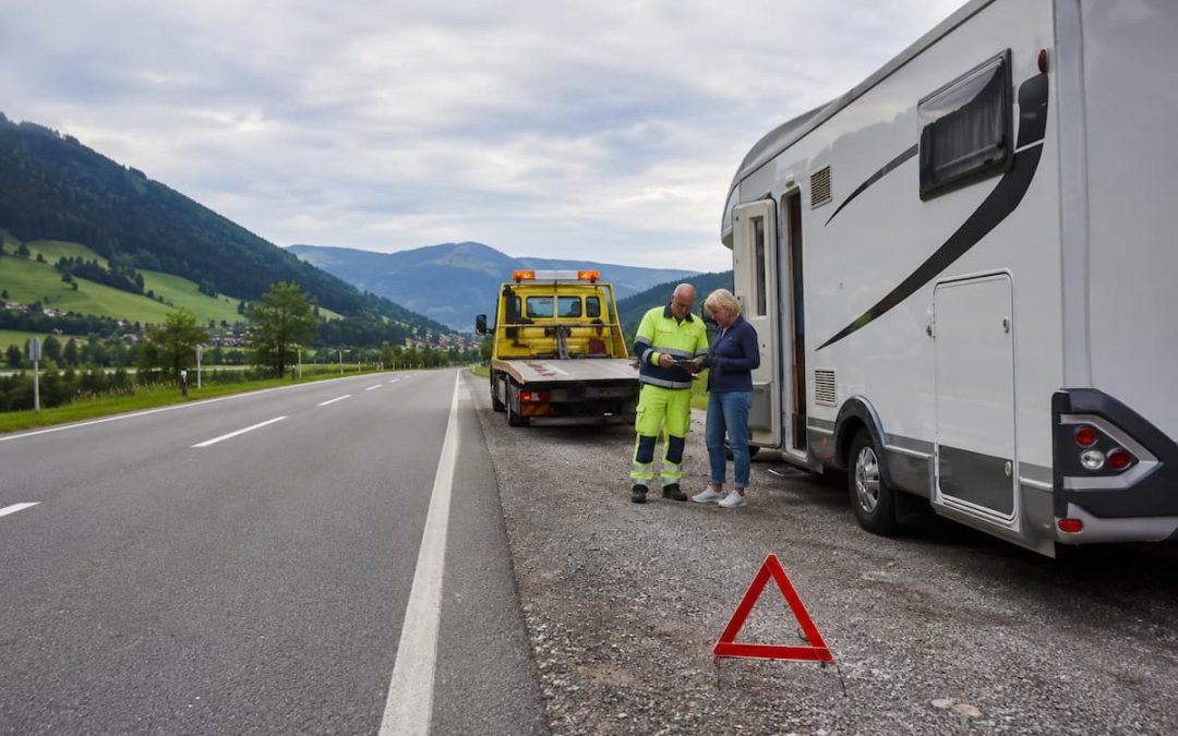 Autocaravana detenida en una carretera europea con grúa y señal de emergencia durante una asistencia en viaje.