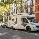 Autocaravana aparcada en una avenida arbolada de la ciudad, compartiendo el espacio público con turismos.